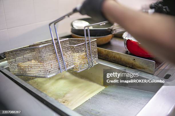 metal fry baskets filled with samosas dripping oil into a deep fryer in a commercial kitchen, highlighting the preparation of a traditional indian dish - samosa stock pictures, royalty-free photos & images