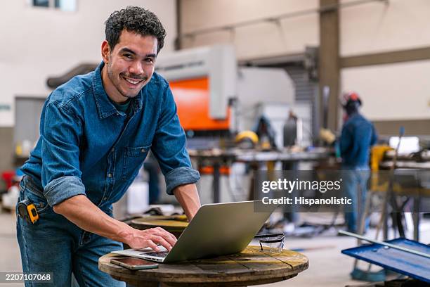 engineer working at a metal factory using a laptop and smiling - switchboard operator stock pictures, royalty-free photos & images