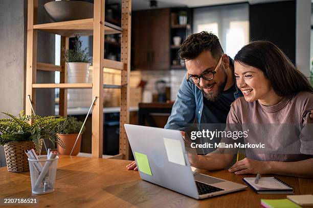 young couple smiling and using laptop at home - sticky-notes-covering-computer-monitor stock pictures, royalty-free photos & images