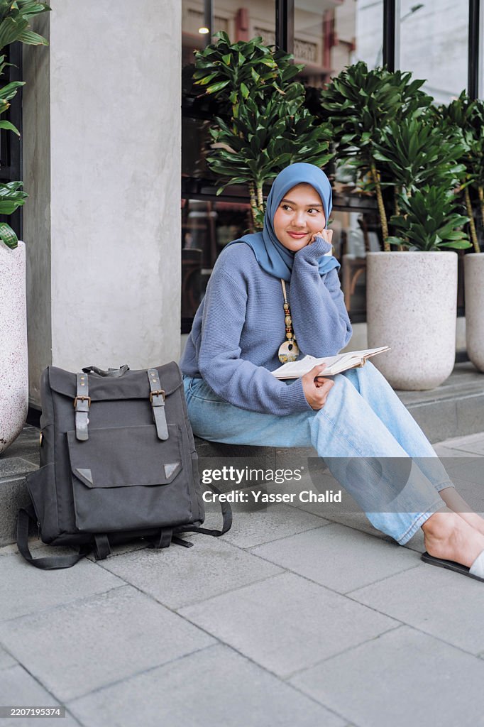 Asian girl waiting for a bus while reading a book