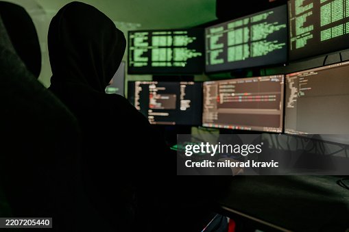 Hacker working on multiple computer screens with green code Hacker working on multiple computer screens with green code