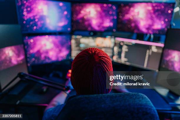 computer programmer working from home with multiple monitors displaying colorful nebulae - web programmer stock pictures, royalty-free photos & images
