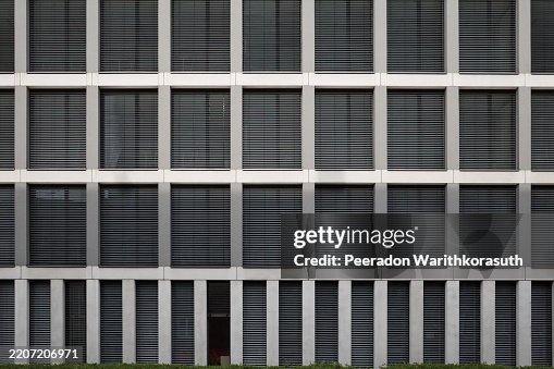 Architectural facade featuring a grid layout of rectangular windows with closed horizontal blinds. Architectural facade featuring a grid layout of rectangular windows with closed horizontal blinds.