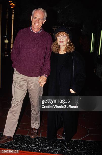 American actor Mike Farrell, wearing a purple sweater over a checked shirt with light grey trousers, and his wife, American actress and singer...