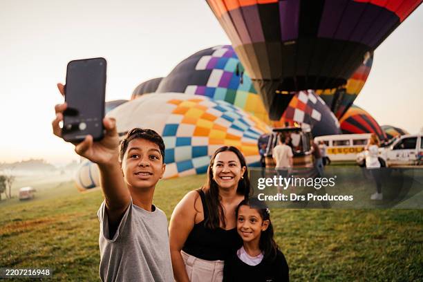 family taking a selfie in front of a hot air balloon. - girl blowing balloon stock pictures, royalty-free photos & images