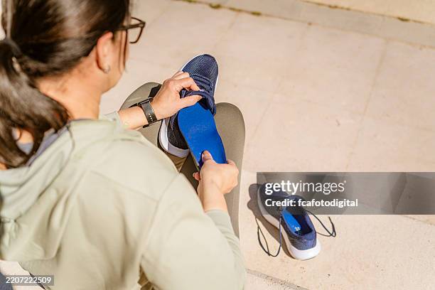 über die schulter aufnahme einer frau, die im freien eine einlegesohle in einen laufschuh einführt - schuhsohle stock-fotos und bilder
