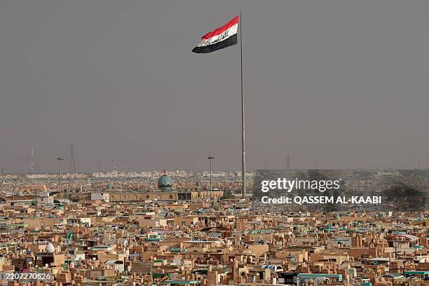 Flag of Iraq flutters above the Wadi-al-Salam cemetery as people visit the tombs of relatives as is customary on the first day of Eid al-Fitr marking...