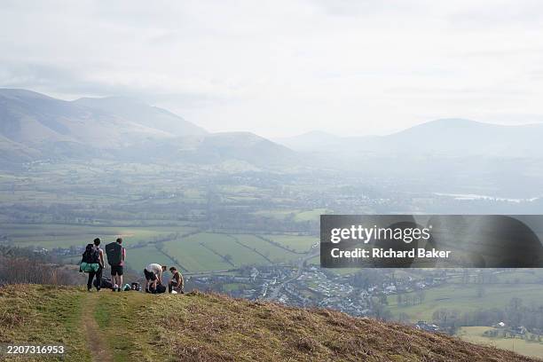 Group of young men pause on a hilltop that overlooks Keswick and distant mountains of the Lake District National Park, on 24th March 2025, in...