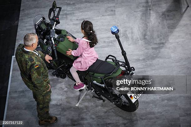 Girl sits on a military motorcycle at the booth of German Federal Armed Forces Bundeswehr during the opening of the Hannover Messe industrial trade...