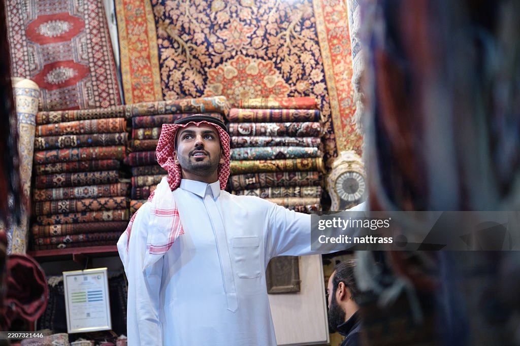 Traditional Saudi Rug Young Saudi Man In Traditional Clothing Browsing Vibrant Handwoven Rugs ...