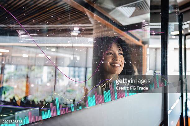 businesswoman looking at data visualizations on glass wall in modern office - forecasting stock pictures, royalty-free photos & images