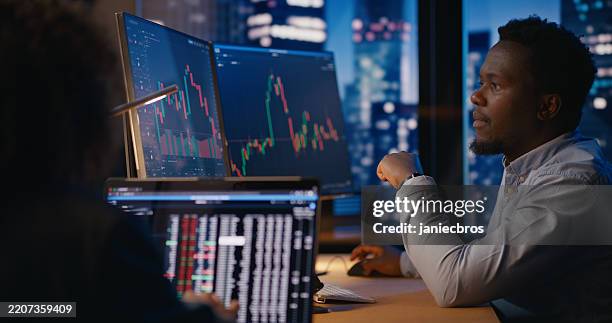 gestore degli investimenti che lavora in ufficio davanti al computer con i grafici del mercato azionario visibili sui display - mercato foto e immagini stock