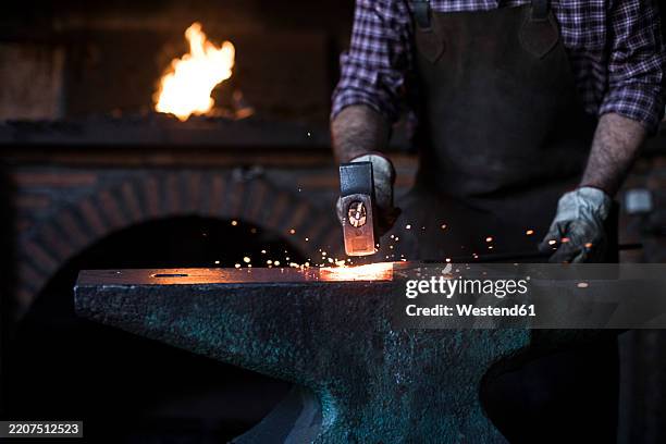 close-up of blacksmith working with hammer at anvil in his workshop - fabbro ferraio foto e immagini stock