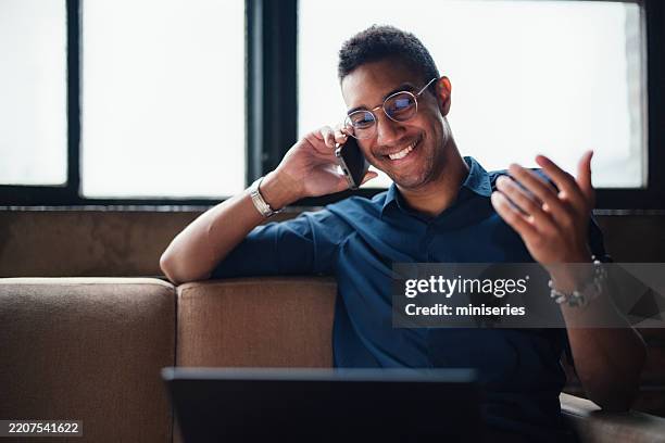 smiling professional man talking on the phone in a modern living room setting - telekommunikationsutrustning bildbanksfoton och bilder