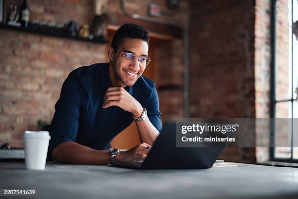 joven profesional que trabaja en una computadora portátil en un entorno de oficina moderno - usar el ordenador fotografías e imágenes de stock