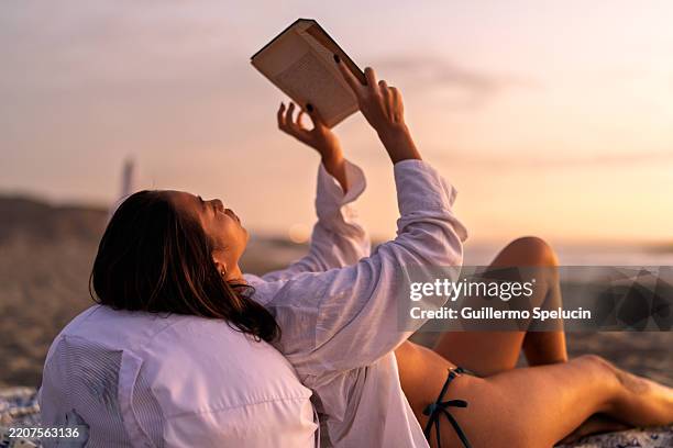 young woman reading a book on the beach at sunset - hot peruvian women stock pictures, royalty-free photos & images