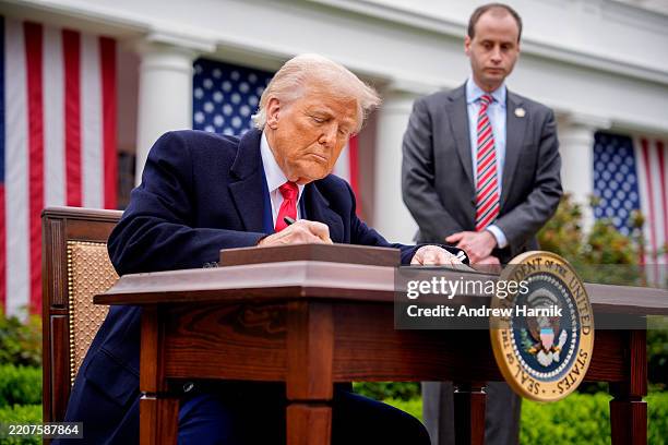 President Donald Trump, accompanied by White House staff secretary Will Scharf, signs executive orders imposing tariffs on imported goods during a...
