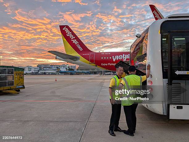 Ground service staff stand next to a shuttle bus beside a VietJet Air aircraft during sunrise at Tan Son Nhat International Airport in Ho Chi Minh...
