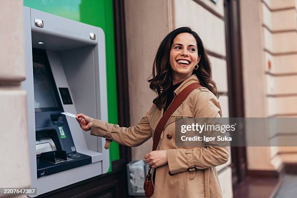 donna sorridente che preleva denaro dal bancomat in città - sportello bancomat foto e immagini stock