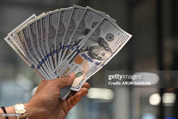 Worker holding US dollars banknotes poses for a photograph at a money exchange outlet in New Delhi on April 3, 2025. US President Donald Trump...