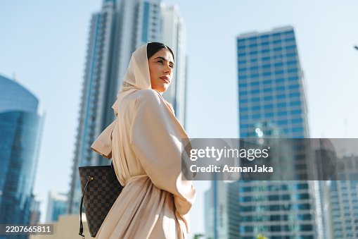 Young Woman in Cream Abaya Standing Against Modern Dubai Skyscrapers Young Woman in Cream Abaya Standing Against Modern Dubai Skyscrapers