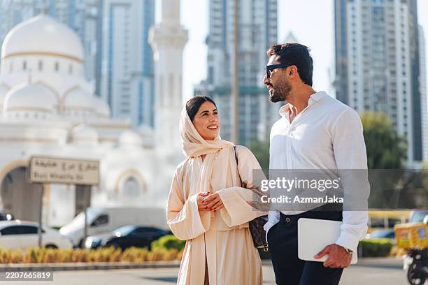 elegantes vielfältiges paar im stadtbild von dubai, das stilvolle neutrale kleidung trägt - oberteil stock-fotos und bilder