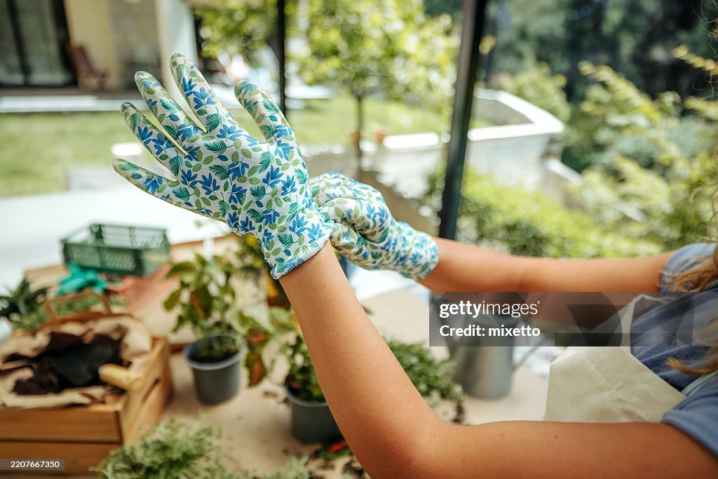 見分けがつかない若い女性がガーデニング用手袋をはめながら、自宅の裏庭で植物の世話をしているクローズアップショット