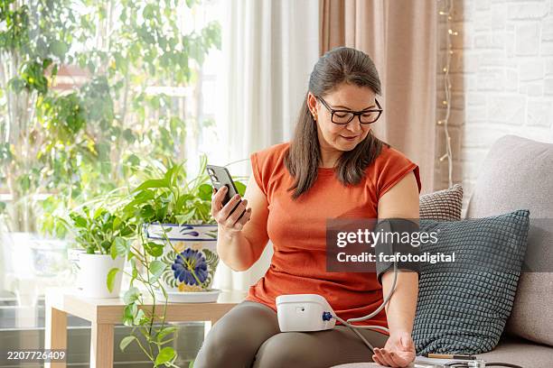 mature woman using phone to talk with her doctor about her blood pressure - blood pressure gauge stock pictures, royalty-free photos & images