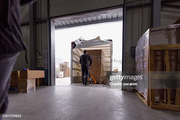 working in distribution warehouse, using pallet jack and moving stack of cardboard boxes with electrical insulation tape - loading dock stock pictures, royalty-free photos & images