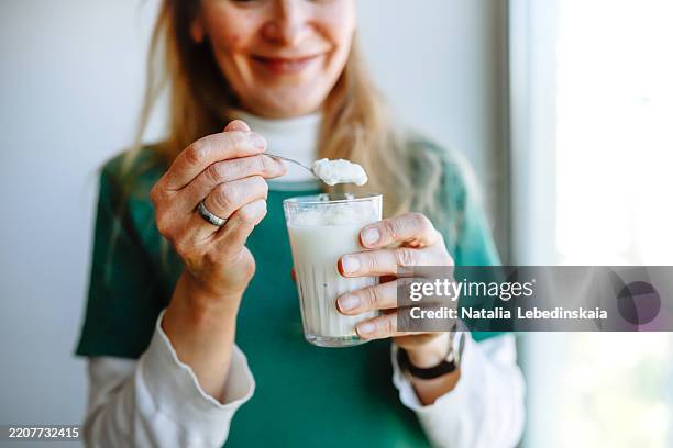 relaxed woman enjoys yogurt and a peaceful morning moment by the window, radiating positivity. - solo una donna anziana foto e immagini stock