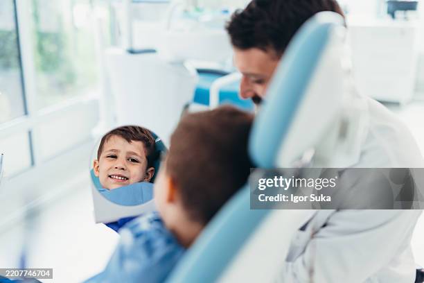 niño mirando sus dientes en el espejo del dentista - espejo dental fotografías e imágenes de stock