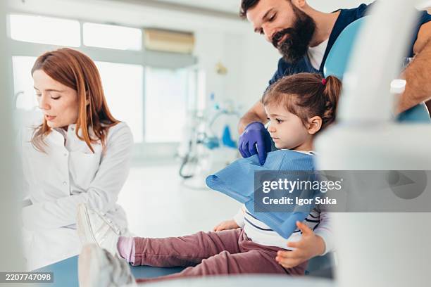 toddler having first dental check up with dentist and nurse assisting - baby bib stock pictures, royalty-free photos & images