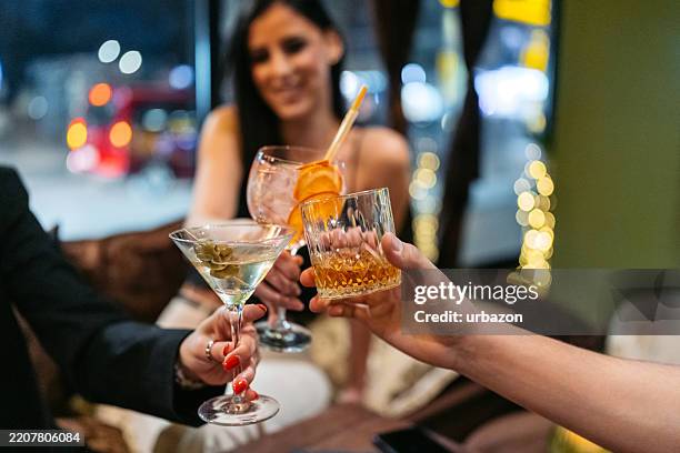 trois jeunes amis portent un toast de célébration avec des cocktails et du whisky dans un bar la nuit - whisky photos et images de collection