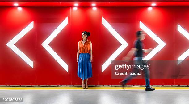 un uomo e una donna che camminano verso le direzioni opposte delle frecce davanti a un muro rosso. conflitto di opinioni, divorzio. - bivio foto e immagini stock