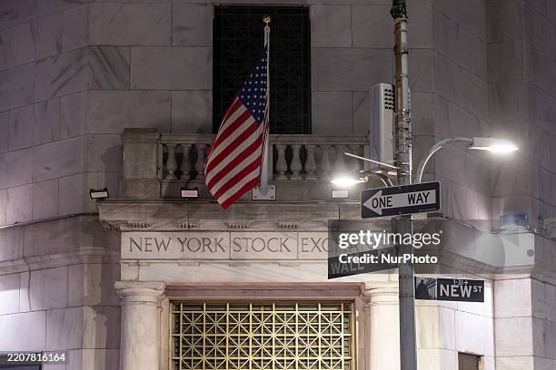 Night view of the illuminated exterior of New York Stock Exchange with a big American flag from the front facade. NYSE building has the style of...
