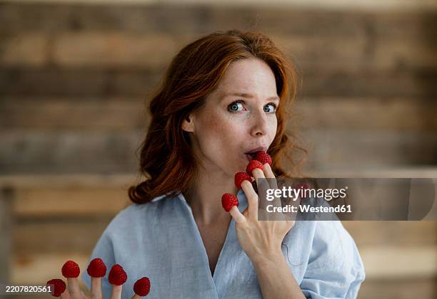 portrait of redheaded woman nibbling raspberries from her fingertips - superfood stock-fotos und bilder