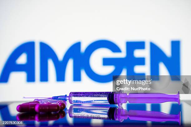 Syringe and some pills are in front of the logo of Amgen pharmaceutical company.