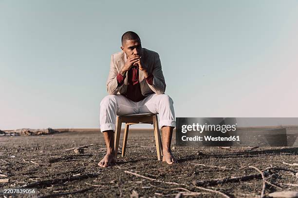 young man sitting on chair in barren land - lost stock pictures, royalty-free photos & images