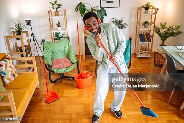 junger mann, der seine wohnung putzt und spaß daran hat, sich so zu verhalten, als würde er mit besen statt mikrofon singen - besen stock-fotos und bilder