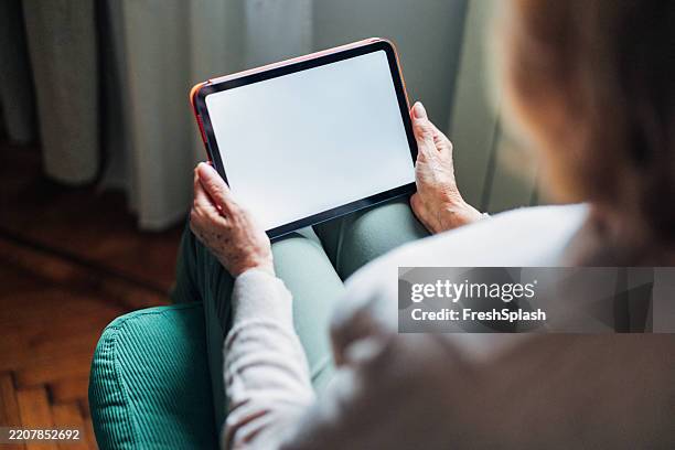 mujer sosteniendo la tableta con la pantalla en blanco en un entorno doméstico relajado - una sola mujer mayor fotografías e imágenes de stock