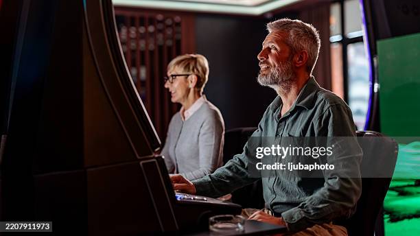 homem maduro e mulher desfrutando de um jogo em uma máquina de jogos de cassino - slot machine 77 - fotografias e filmes do acervo