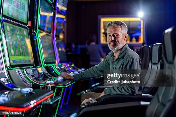 l’homme aime jouer aux machines à sous dans un environnement de casino luxueux - casino interior photos et images de collection