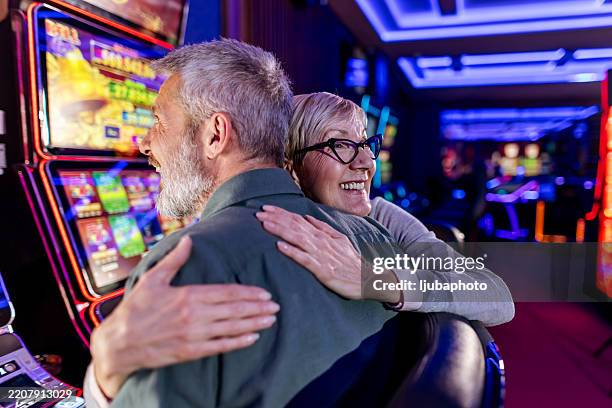 happy couple playing slot machines in a vibrant casino environment - casino table games stockfoto's en -beelden