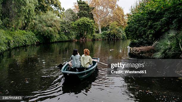 lesbian couple rowing boat amidst trees in lake at ciutadella park, barcelona, spain - rowing boat stock pictures, royalty-free photos & images