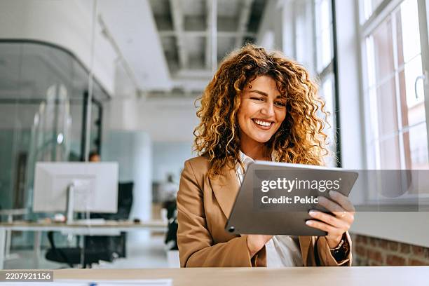 junge fröhliche geschäftsfrau, die im büro an einem digitalen tablet arbeitet - tablet stock-fotos und bilder