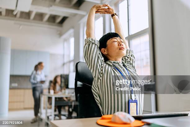 mujer estirándose mientras trabaja en la oficina - hacer un descanso fotografías e imágenes de stock