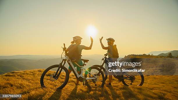 cyclists high-five at mountain summit during sunset - cyclist mountain stock pictures, royalty-free photos & images