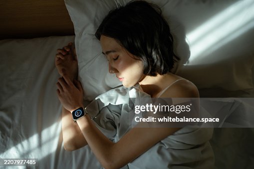 Woman sleeping peacefully in bed, wearing a smart watch to track her sleep Woman sleeping peacefully in bed, wearing a smart watch to track her sleep