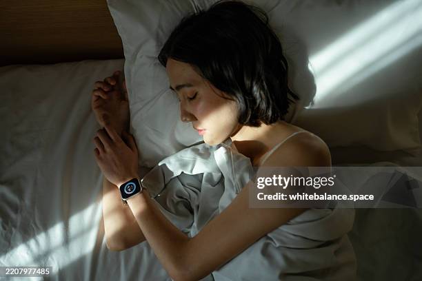 woman sleeping peacefully in bed, wearing a smart watch to track her sleep - rapariga no quarto tecnologia imagens e fotografias de stock