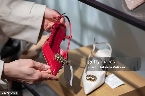 hands examining a stylish red high heel shoe in a boutique - knöchelriemen schuh stock-fotos und bilder